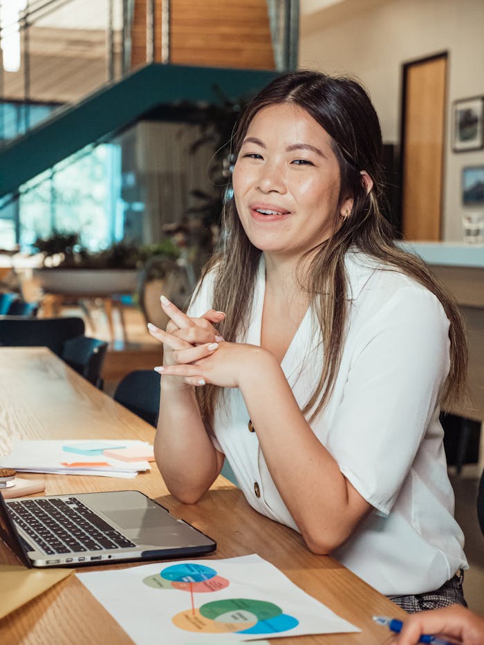 A woman smiling at a workspace, sitting with a laptop and colorful charts.